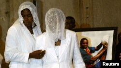 FILE - The wife, Marie-Louise Foe (C), and mother (L), of the late Cameroon player Marc-Vivien Foe, walk past his picture during his funeral ceremony.