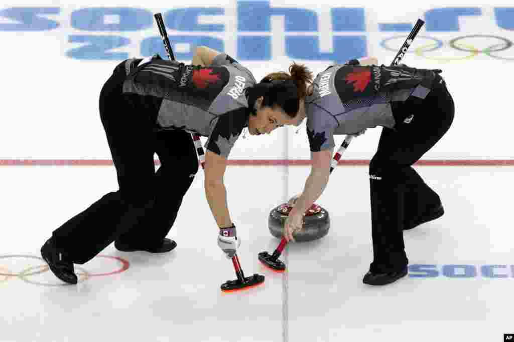 Canada's Jill Officer, left, and Dawn McEwen, right, sweep the ice during the women's curling competition against Denmark at the 2014 Winter Olympics, Feb. 13, 2014.