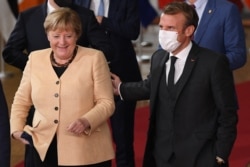 Germany's Chancellor Angela Merkel , left, reacts next to France's President Emmanuel Macron as they pose for a family photograph with EU leaders on the first day of a European Union summit at The European Council Building in Brussels, October 21, 2021.