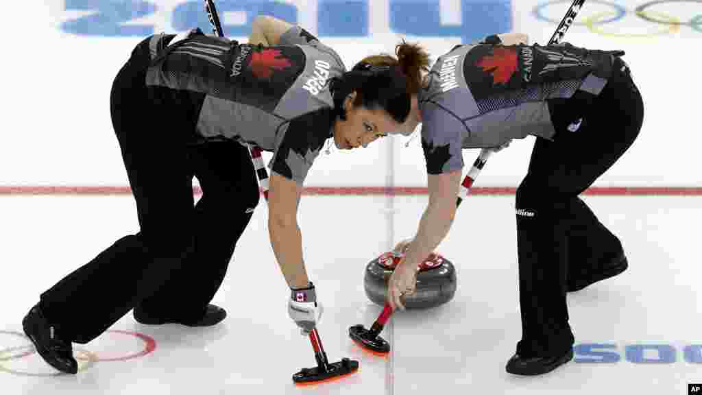 Canada's Jill Officer, left, and Dawn McEwen, right, sweep the ice during the women's curling competition against Denmark at the 2014 Winter Olympics, Feb. 13, 2014.