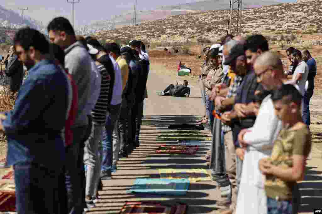 A Palestinian protester waves a national flag, as others proform the Friday prayers during a demonstration against the establishment of Israeli outposts on their lands, in Beit Dajan, east of Nablus in the Israeli-occupied West Bank.