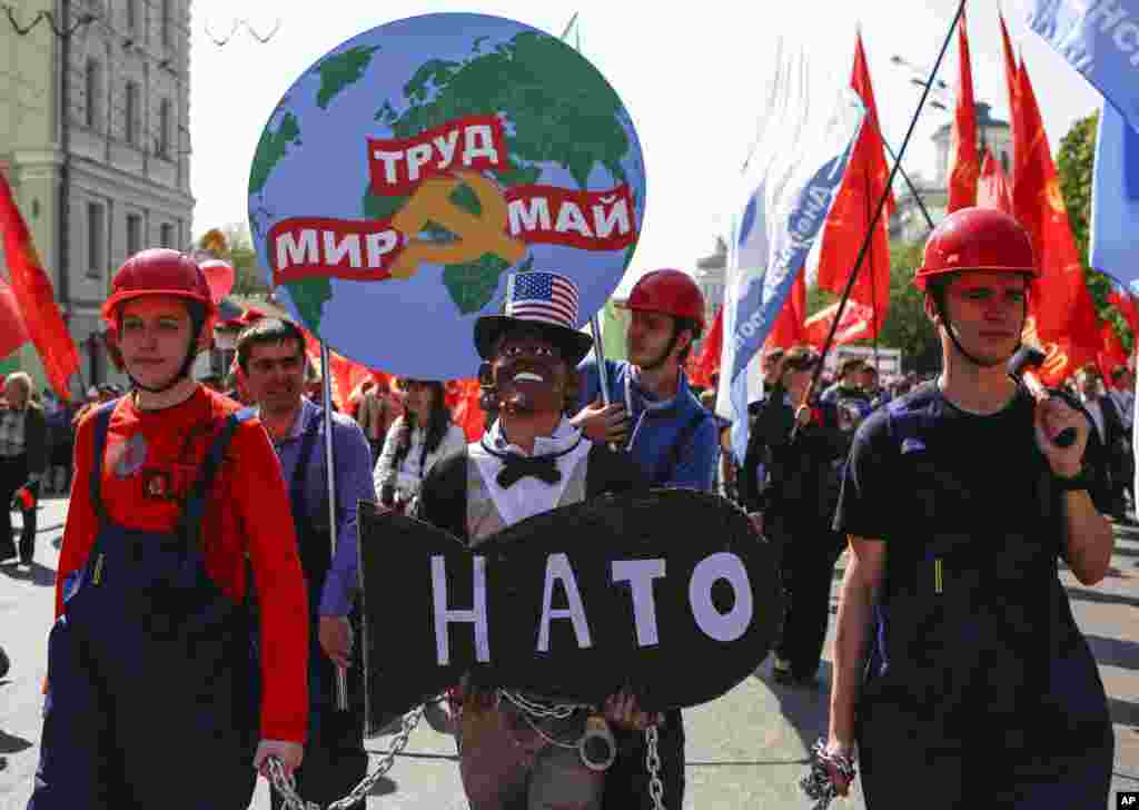 People in helmets dressed as Russian factory workers hold a man wearing a Barack Obama mask in chains as they take part in a Communists demonstration in downtown Moscow, May, 1, 2014.