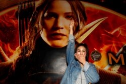 FILE PHOTO: Student Natchacha Kongudom flashes a three-finger salute inspired by the movie "The Hunger Games" in front of a billboard of the film outside the Siam Paragon cinema in Bangkok November 20, 2014.