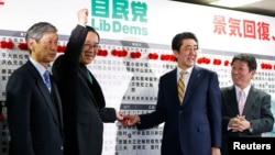 Liberal Democratic Party (LDP) Secretary-General Sadakazu Tanigaki, center left, gestures next to Japan's Prime Minister Shinzo Abe, center right, as they pose during an election night event at the LDP headquarters in Tokyo, Dec. 14, 2014. 