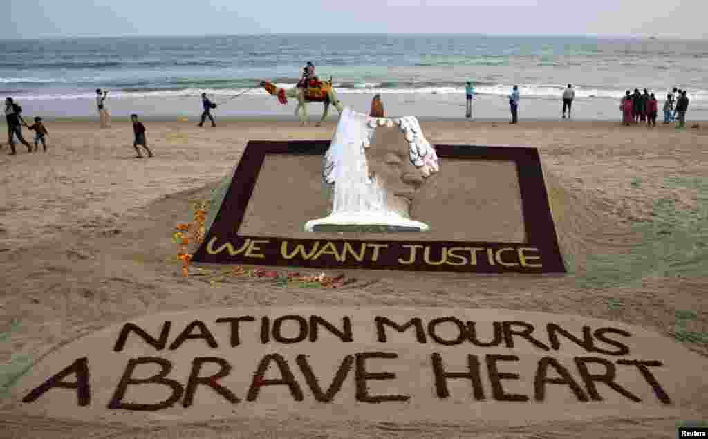People walk near a sand sculpture with the words &quot;We Want Justice&quot; created by Indian sand artist Sudarshan Patnaik, in solidarity with a gang rape victim who was assaulted in New Delhi, on a beach in the eastern Indian state of Odisha, December 29, 2012. 
