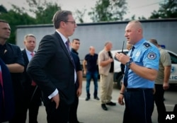 In this photograph made available by the Serbian Presidency, a Kosovo police officer speaks to Serbia's president Aleksandar Vucic, left, to say he cannot continue his trip to the village of Banje due to roadblocks, in Zubin Potok, Kosovo, Sept. 9, 2018.