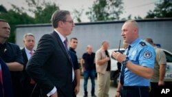 In this photograph made available by the Serbian Presidency, a Kosovo police officer speaks to Serbia's president Aleksandar Vucic, left, to say he cannot continue his trip to the village of Banje due to roadblocks, in Zubin Potok, Sept. 9, 2018.