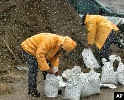In this photo taken through a glass window, released by Santa Barbara County Fire Department, people fill up sandbags under the rain in Santa Barbara, California, Jan. 8, 2018.