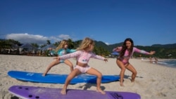 Rayana Tanimoto teaches her five-year-old twin daughters Eloa, left, and Ayla, how to surf, at Maresias beach, in Sao Sebastiao, Brazil, Nov. 27, 2021.