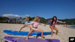 Rihanna Donimoto ensina suas filhas gêmeas de cinco anos, Elova e Ayla, a surfar, no dia 27 de novembro de 2022, na praia de Maurício, em São Sebastião, Brasil.