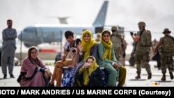 کابل ائیرپورٹ پر ایک افغان خاندان انخلا کے لیے فلائٹ کا انتظار کر رہا ہے۔ پس منظر میں امریکی فوجی ائیرپورٹ کی سیکیورٹی کے فرائض سرانجام دے رہے ہیں۔ 19 اگست 2021