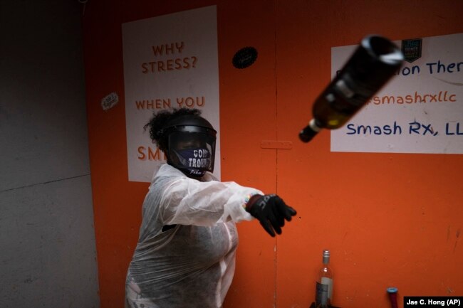 La Shaun Aaron, 43, throws a wine bottle into a wall during a session to help relieve stress at Smash Rx, Feb. 5, 2021. (AP Photo/Jae C. Hong)