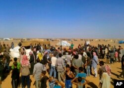 FILE - People gather to take basic foodstuffs and other aid from community leaders charged with distributing equitably the supplies to the Rukban refugee camp on the Jordan-Syria border, Aug. 4, 2016.