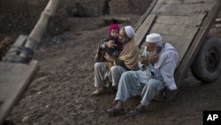 FILE - An elderly Afghan refugee trims his beard while another plays with his grandson on the outskirts of Islamabad, Pakistan, Feb. 19, 2015.