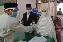 Bride Karlina and groom Cahya Sudrajat receive their marriage certificate from Muslim officiant Solehchudin while all wear protective gears to prevent the spread of the coronavirus during a wedding ceremony in Jakarta, Indonesia, Friday, June 19, 2020. (AP)