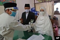 La mariée Karlina et le marié Cahya Sudrajat reçoivent leur certificat de mariage du célébrant musulman Solehchudin alors que tous portent des équipements de protection pour empêcher la propagation du coronavirus lors d'une cérémonie de mariage à Jakarta, en Indonésie, le vendredi 19 juin 2020 (AP)