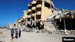 FILE - Youths walk past buildings that were destroyed during clashes between Libyan forces and Islamic State militants in Sirte, Libya, Nov. 1, 2017.