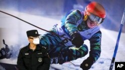 FILE - A police officer wearing a face mask and goggles to protect against COVID-19, stands near a poster of a skier on the wall at a train station in Zhangjiakou in northern China's Hebei Province, Friday, Nov. 26, 2021. (AP Photo/Mark Schiefelbein, File