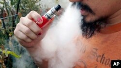 FILE - A man blows a puff of smoke as he vapes with an electronic cigarette, Oct. 18, 2019. 