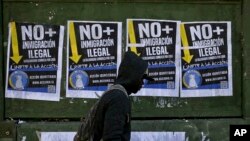 A migrant walks past anti-migrant posters that read in Spanish "No more illegal immigration. Solidarity begins at home" prior to a march in favor of migrants, organized by the National Immigrants Coordinator, in Santiago, Chile, Aug. 20, 2017. 