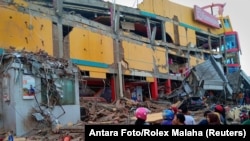 Người dân đứng trước một trung tâm mua sắm đổ sập sau khi một trận động đất làm rung chuyển thành phố Palu, đảo Sulawesi, Indonesia, ngày 29 tháng 9, 2018.