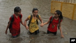 FILE - Indian girls hold hands and wade through a waterlogged street .