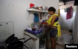 Daniele Santos carries her baby, Juan Pedro, who has microcephaly, in a sling while washing dishes in her home in Recife, Brazil, March 26, 2016.