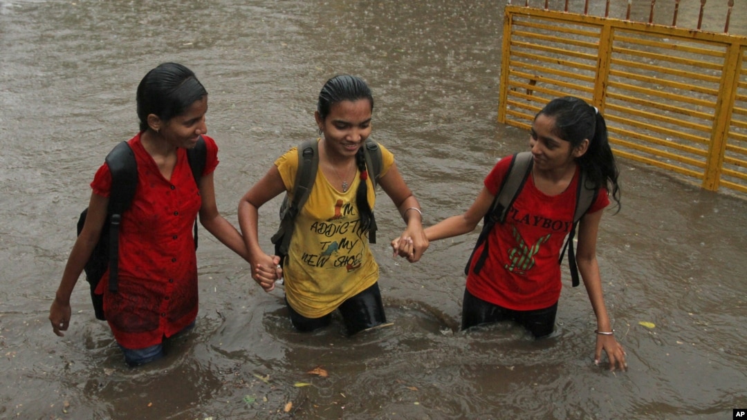FILE - Indian girls hold hands and wade through a waterlogged street .
