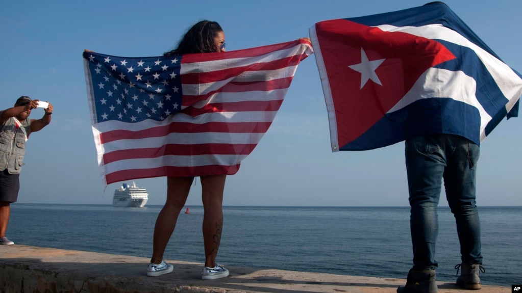 FILE - Yaney Cajigal, left, and Dalwin Valdes display flags for the U.S. and Cuba while awaiting the arrival of a Carnival cruise ship from Miami to Havana, Cuba, May 2, 2016. The Florida Straits had been closed to most U.S.-Cuba traffic for decades.