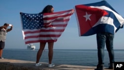FILE - Yaney Cajigal, left, and Dalwin Valdes display flags for the U.S. and Cuba while awaiting the arrival of a Carnival cruise ship from Miami to Havana, Cuba, May 2, 2016. The Florida Straits had been closed to most U.S.-Cuba traffic for decades.