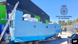 In this photo provided by the Spanish National Police, March 12, 2021, a homemade semi-submersible submarine sits outside a warehouse in Malaga, Spain. 