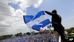 FILE - A man waves a Nicaraguan flag as people participate in a demonstration called the "March of the Flowers" remembering the children killed during the last two months of violence, in Managua, Nicaragua, June 30, 2018. The Central American nation has been rocked since mid-April by chaos as protesters maintaining roadblocks and demanding Ortega's ouster are met by a heavy-handed crackdown by security forces and allied civilian groups.