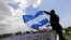 FILE - A man waves a Nicaraguan flag as people participate in a demonstration called the "March of the Flowers" remembering the children killed during the last two months of violence, in Managua, Nicaragua, June 30, 2018. The Central American nation has been rocked since mid-April by chaos as protesters maintaining roadblocks and demanding Ortega's ouster are met by a heavy-handed crackdown by security forces and allied civilian groups.