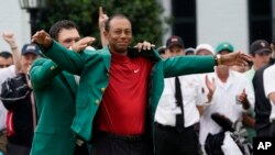Patrick Reed helps Tiger Woods with his Masters green jacket after Woods won the Masters golf tournament, April 14, 2019, in Augusta, Ga. 