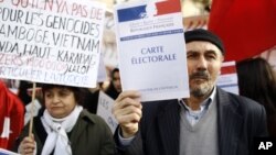 Turkish citizens in France, one of them holding a booklet reading "Electoral card", demonstrate in front of the Senate to protest against a law that would make it a crime to deny "genocide" of Armenians, in Paris, Monday, Jan. 23, 2012.