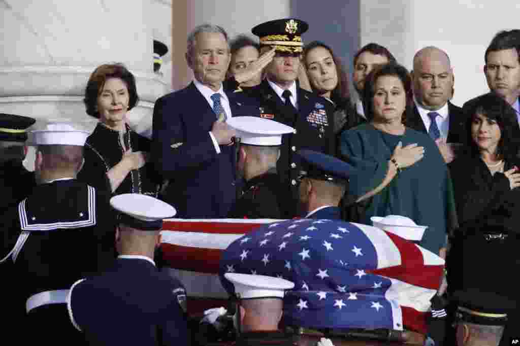 Former President George W. Bush, Laura Bush, left, and other family members watch as the flag-draped casket of former President George H.W. Bush is carried by a joint services military honor guard to lie in state in the rotunda of the U.S. Capitol, Dec. 3