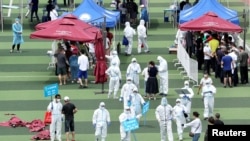 Medical workers in protective suits help people lining up inside a sports center for nucleic acid tests, following new cases of coronavirus disease (COVID-19) in Beijing, China, June 15, 2020.