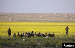 Fighters from the Syrian Democratic Forces stand near a group of men, near Baghuz, Deir el-Zour province, Syria, March 6, 2019.