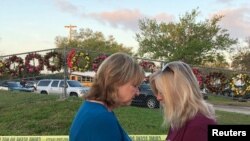 Beverly Turner and Michele Brown huddle to pray in front of a fence decorated with wreaths as students and faculty arrive at Marjory Stoneman Douglas High School for the first time since the mass shooting in Parkland, Florida, Feb. 28, 2018. 