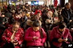 Passengers use their smartphones as they sit in a waiting room at the Beijing Railway Station in Beijing, Jan. 30, 2016.