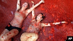 Two woman lie in a puddle of squashed tomatoes during the annual "tomatina" tomato fight fiesta, in the village of Bunol, 50 kilometers outside Valencia, Spain, Wednesday, Aug. 26, 2015. 