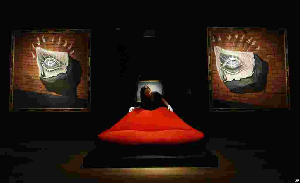 A Christie&#39;s employee adjusts a sofa called &#39;Mae West Lips Sofa&#39; made by Salvador Dali and Edward James, in front of Salvador Dali&#39;s paintings &#39;L&#39;oiel fleuri, decor pour le ballet Trist&#39; at Christie&#39;s in London.&nbsp; The paintings and the sofa belong to a sale set for Tuesday.