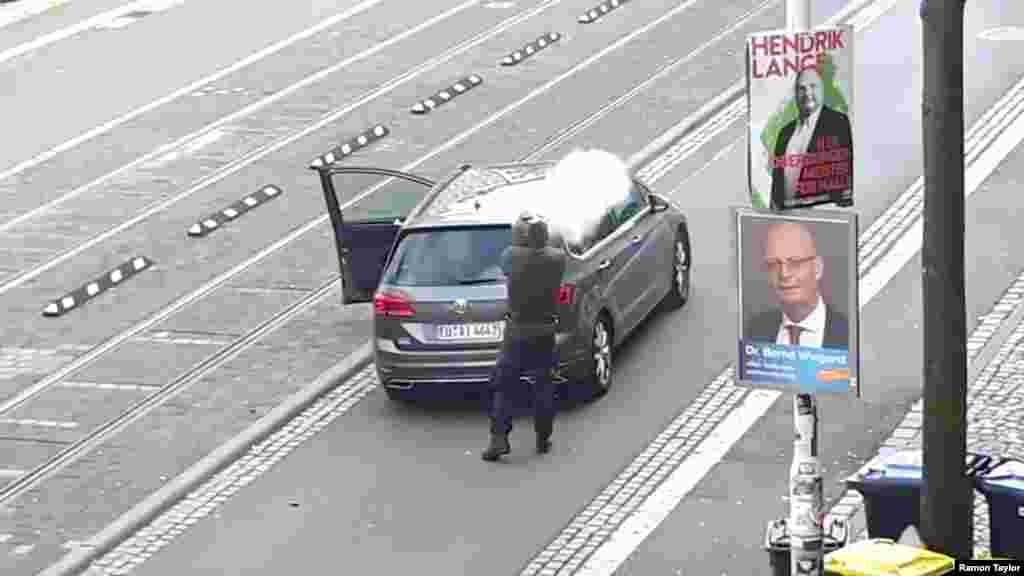 A man shoots a firearm from behind a grey car in Halle, Germany, in this amateur video still image. Two people were killed in shooting attacks on a synagogue and a nearby kebab shop in the eastern German city. One suspect was arrested, but two others fled in a hijacked a car, officials said.