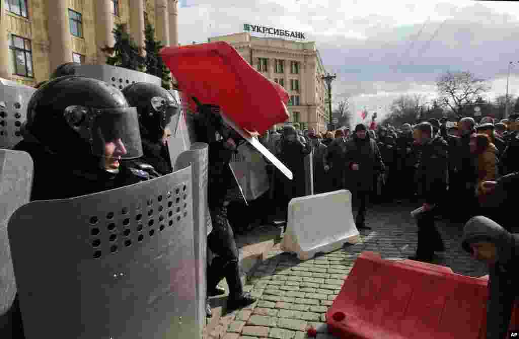 A Ukrainian riot police officer tries to shield himself from a road block thrown by pro-Russia supporters near the regional administrative building during a rally in Kharkiv, Ukraine, March 16, 2014. 