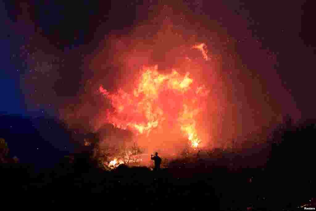 A firefighter tries to extinguish a fire as a wildfire burns near the village of Gavalas, in Evia, Greece, July 6, 2019.