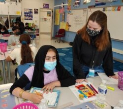 Substitute teacher Sophie Carter helps a student at McNair Upper Elementary School, in Herndon, Fairfax County, Virginia. (Deborah Block/VOA)