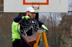 Un empleado de Obras Públicas de Pittsburgh retira un aro de baloncesto de una cancha en el lado norte de Pittsburgh, el lunes 30 de marzo de 2020.