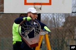 Un empleado de Obras Públicas de Pittsburgh retira un aro de baloncesto de una cancha en el lado norte de Pittsburgh, el lunes 30 de marzo de 2020.