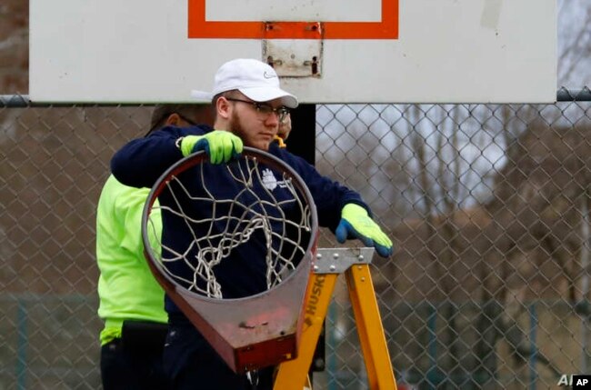 Un empleado de Obras Públicas de Pittsburgh retira un aro de baloncesto de una cancha en el lado norte de Pittsburgh, el lunes 30 de marzo de 2020.