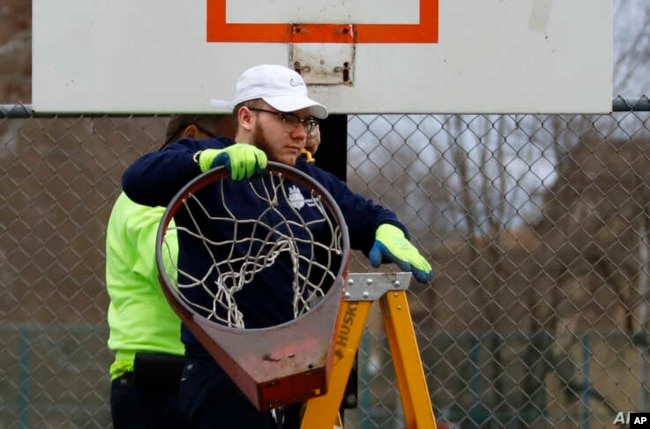 Un empleado de Obras Públicas de Pittsburgh retira un aro de baloncesto de una cancha en el lado norte de Pittsburgh, el lunes 30 de marzo de 2020.